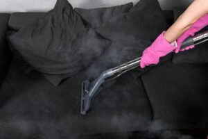 cropped shot of person in rubber gloves cleaning sofa with vacuum cleaner and hot steam